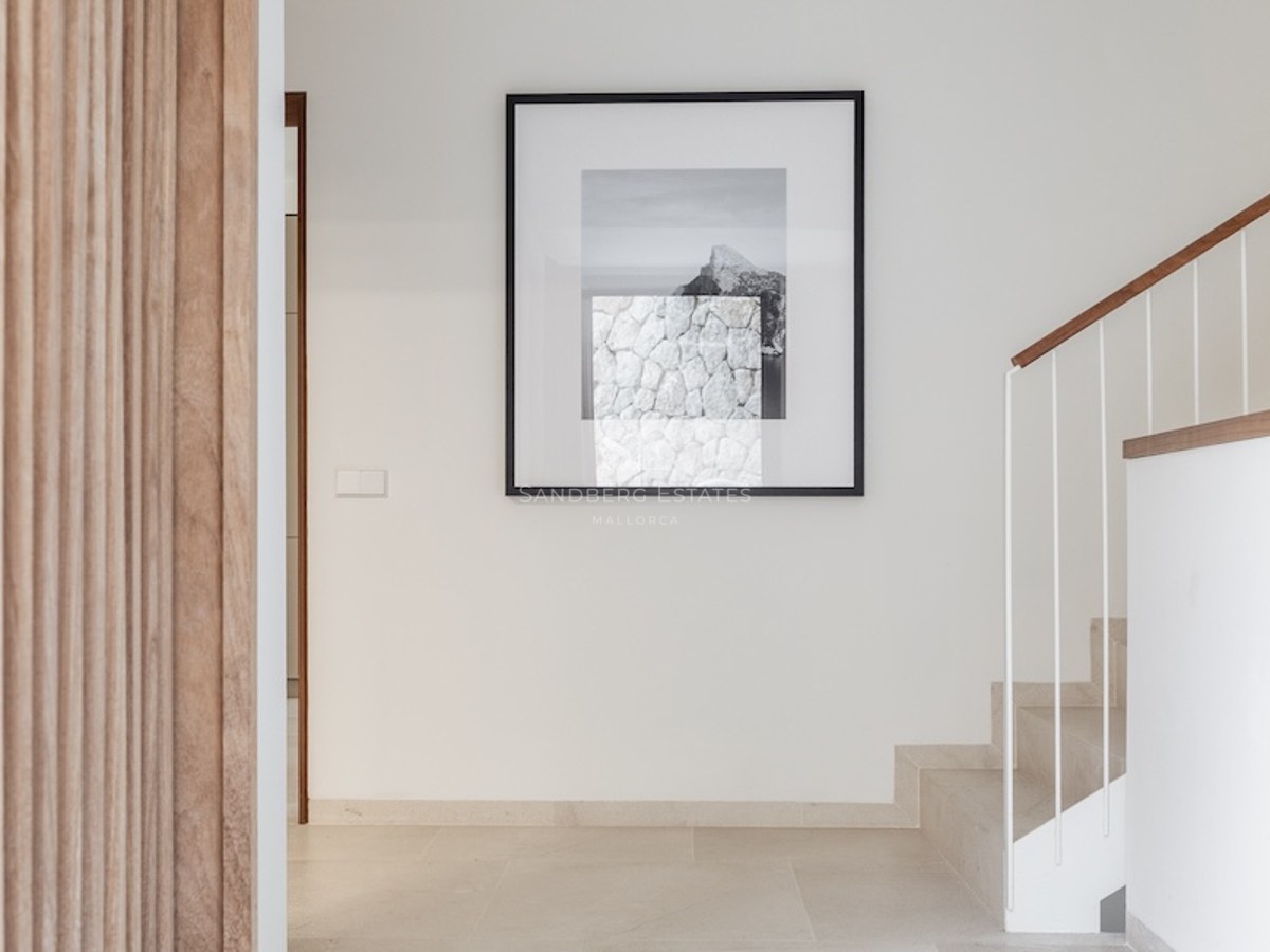 Minimalist hallway with stone stairs, a wooden handrail, and a large framed artwork on a white wall.