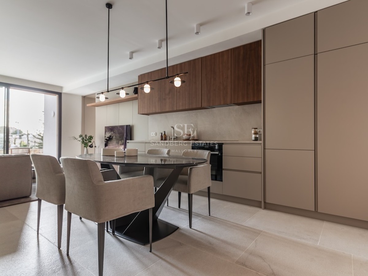 Modern dining area with an oval dark marble table, beige chairs, and a minimalist kitchen with wood accents.