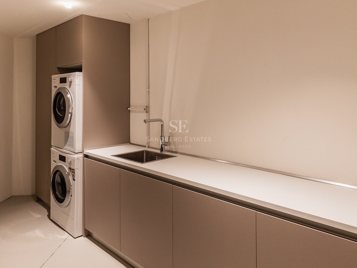 Modern laundry room with stacked washer and dryer, long white countertop, and integrated stainless steel sink.