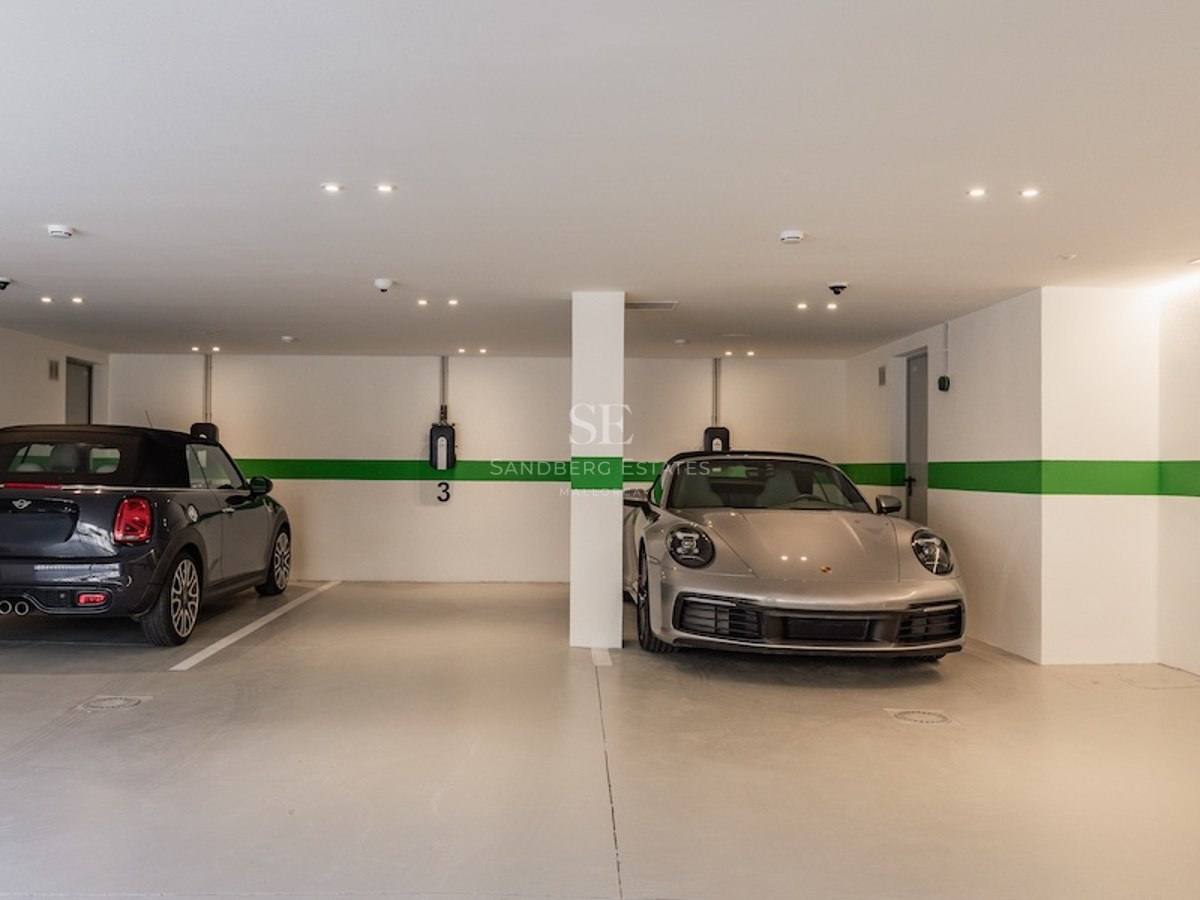 Modern underground parking garage with white walls, green stripes, two cars, and electric vehicle charging points.