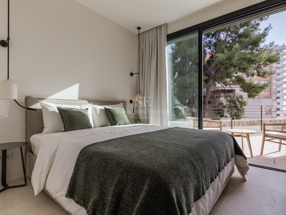 Bright bedroom featuring a double bed with green accents and large glass sliding doors opening to a terrace.