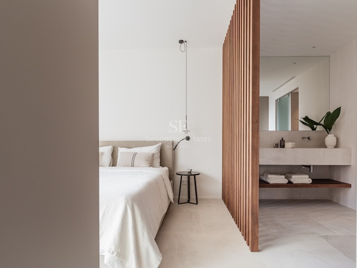 Modern bedroom with a beige bed and a wooden slat divider separating a stone vanity bathroom area.