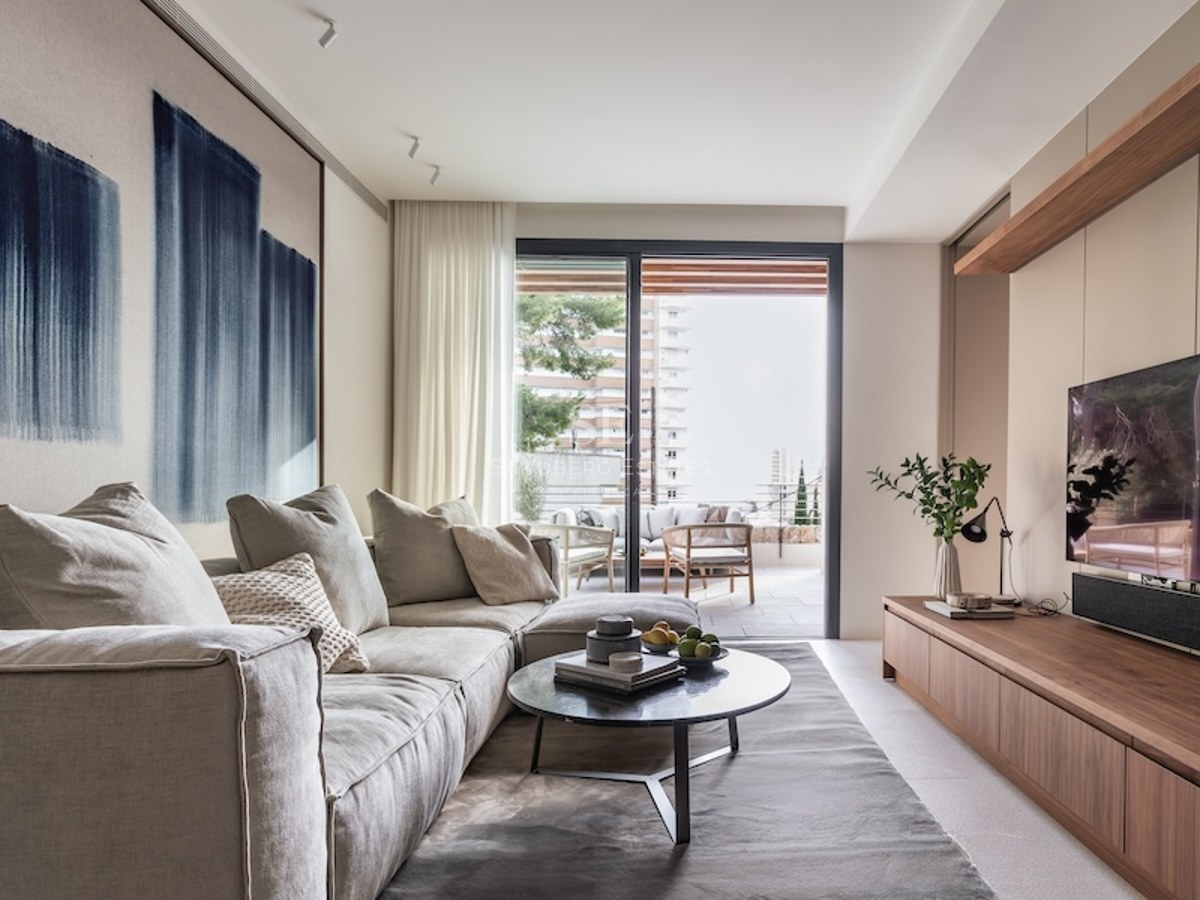 Modern beige sofa in a sunlit living room with wood furniture and a large sliding glass door opening to a terrace.