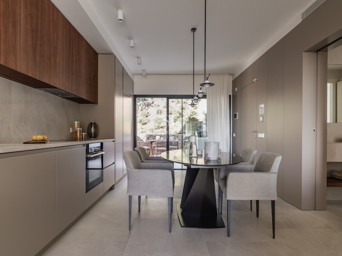 Minimalist kitchen with taupe and wood cabinetry, a grey dining table, and large glass doors leading to a terrace.