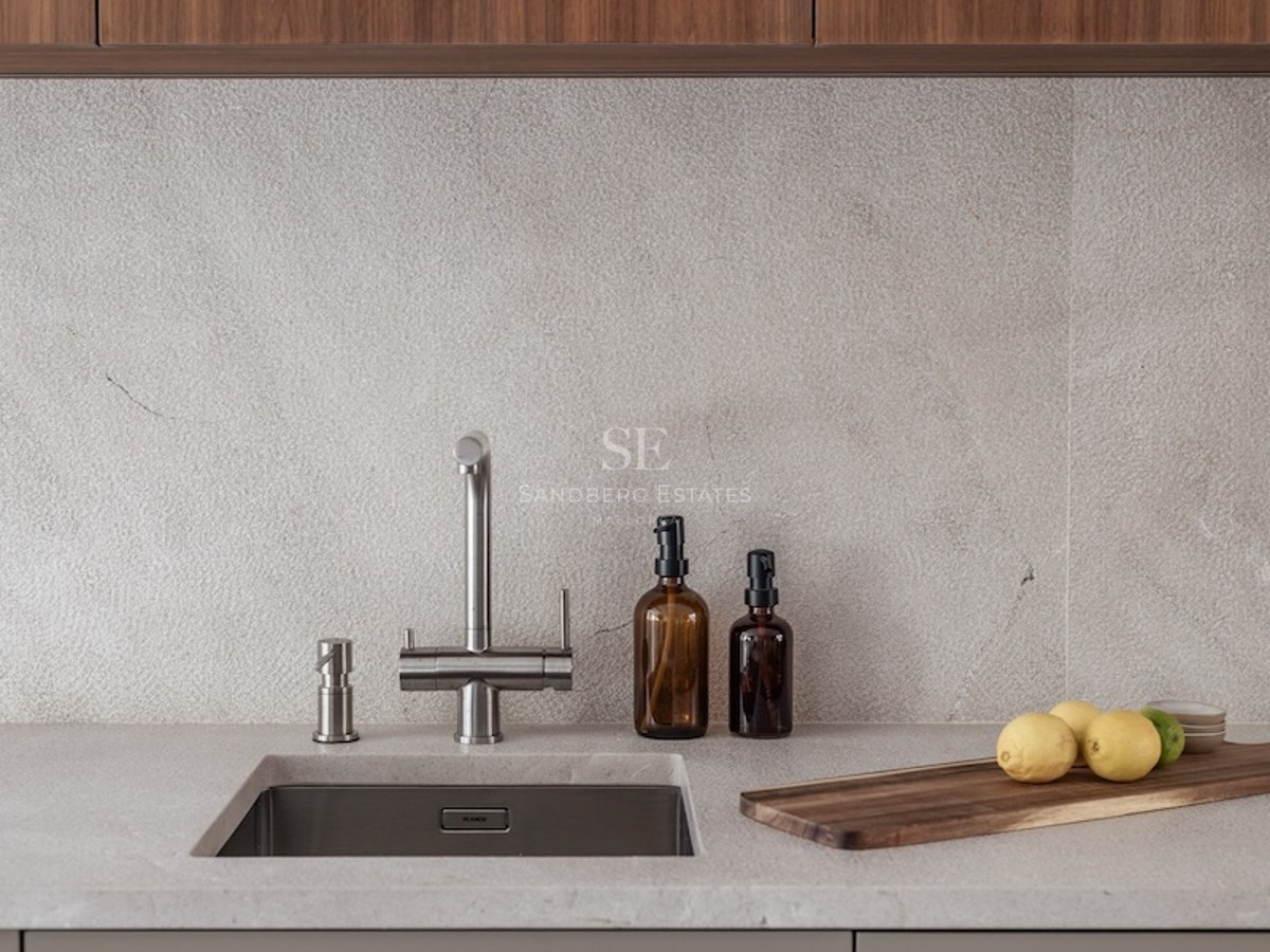 Close-up of a kitchen sink with a stainless steel faucet, stone countertop, and wooden cutting board.