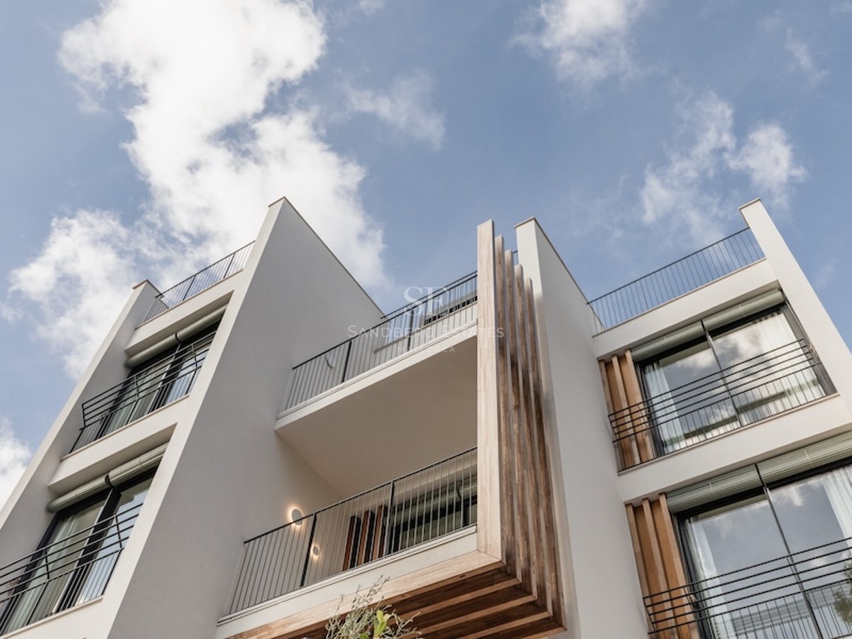 Low-angle view of a modern white building facade with wooden accents and black balcony railings against a blue sky.
