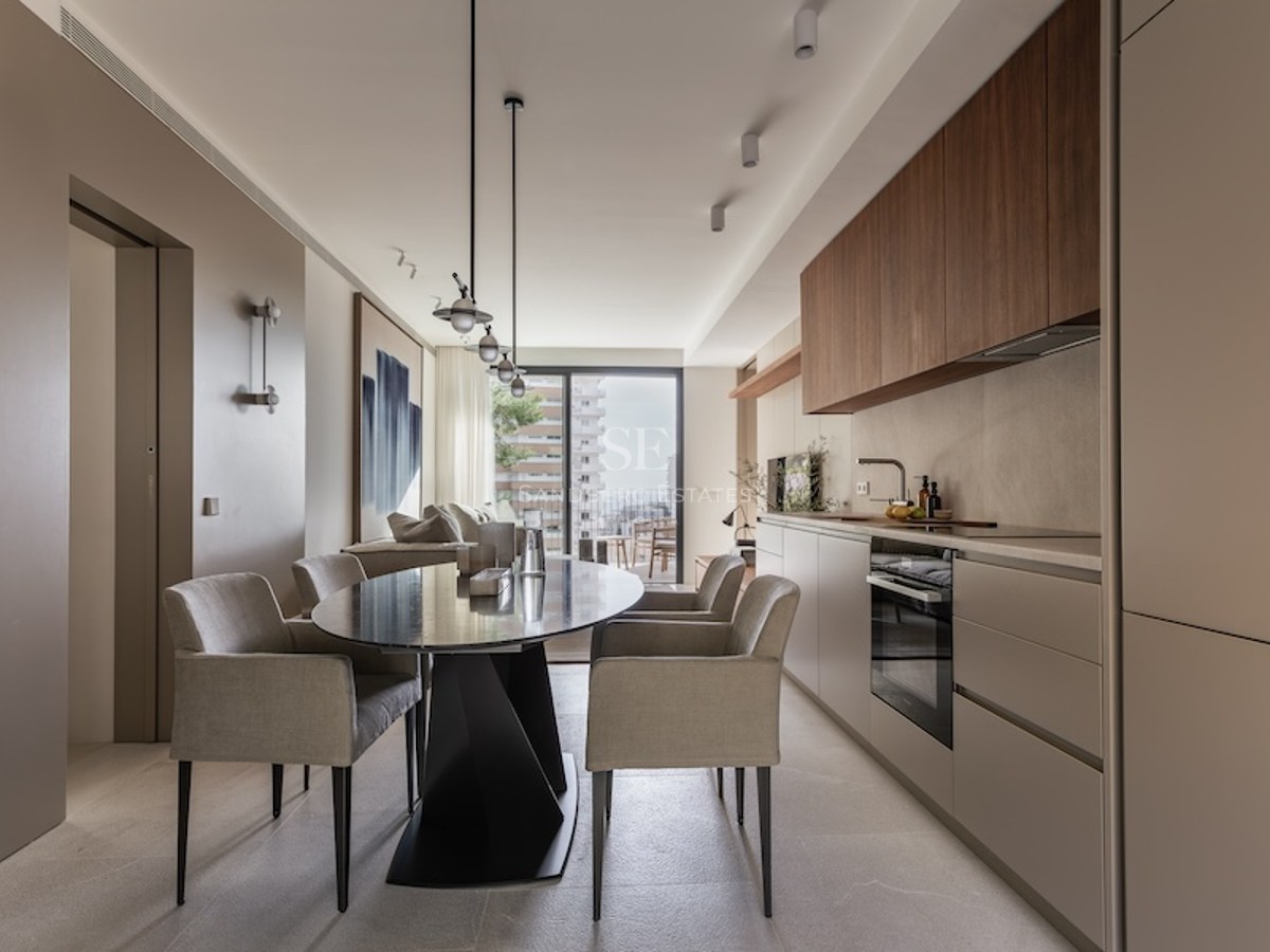 Contemporary dining room with oval black table, grey chairs, and a minimalist integrated kitchen with balcony access.