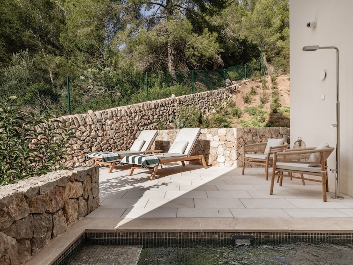 Modern stone terrace featuring designer sun loungers, a metallic outdoor shower, and views of a lush forest.