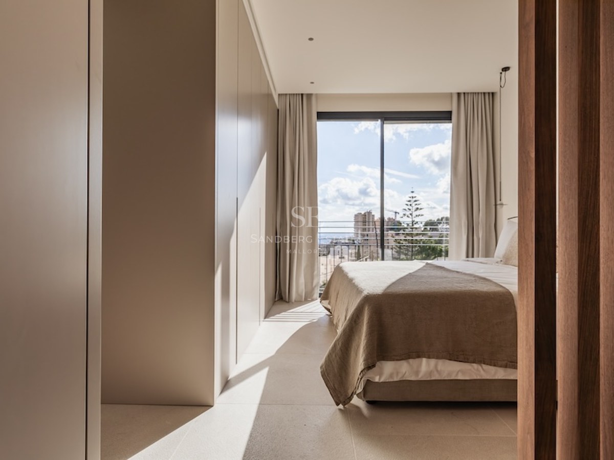 Modern bedroom with beige bedding, built-in wardrobes, and a large sliding glass door opening to a city balcony.