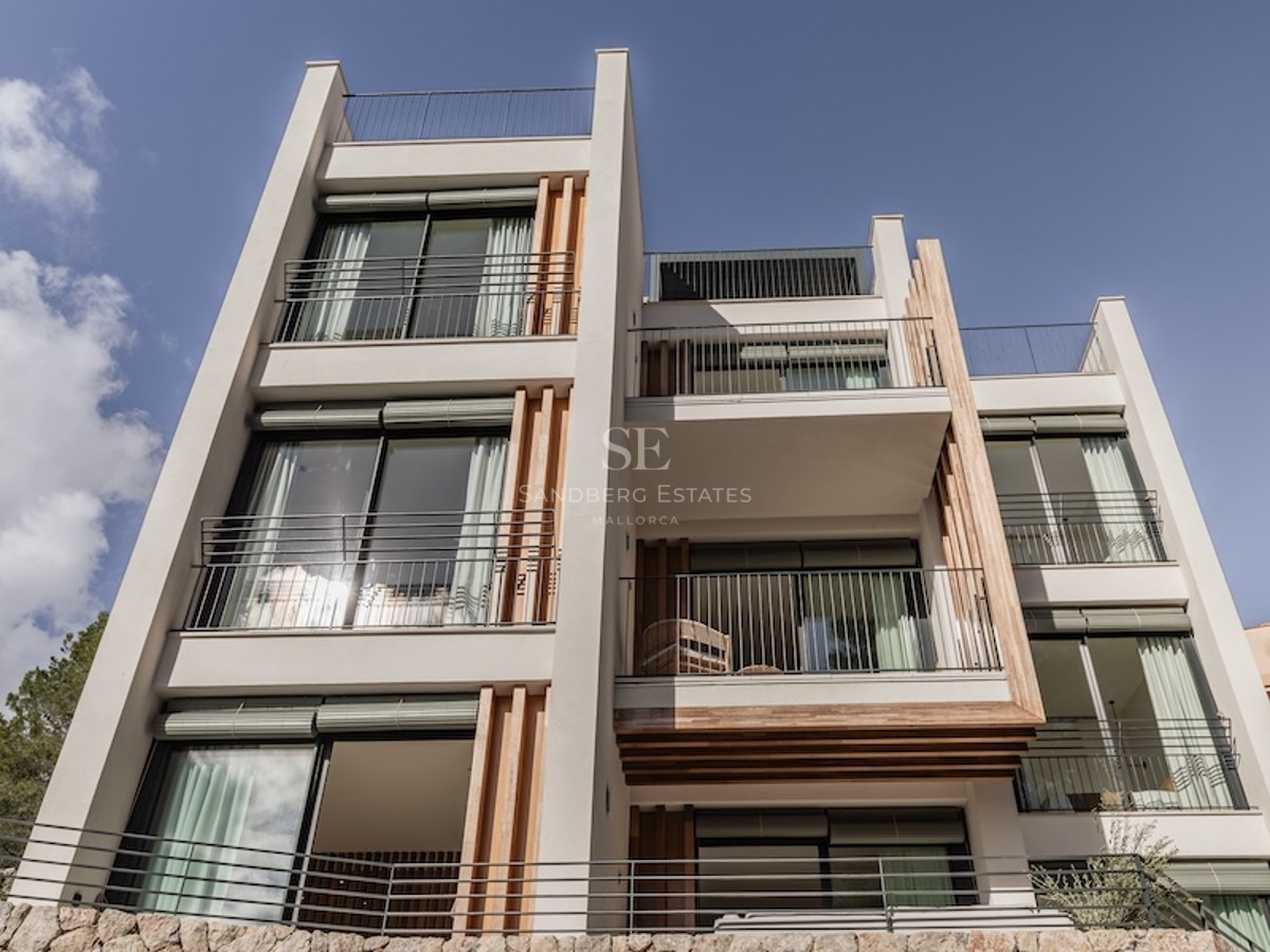 Low-angle view of a white modern villa with wooden slats, large glass windows, and black metal balconies against a blue sky.