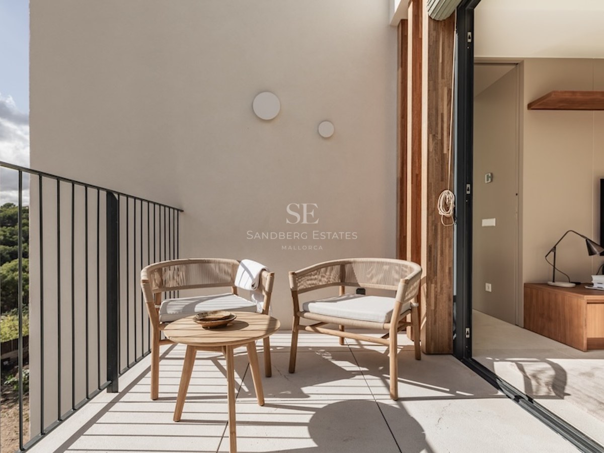 Sunlit balcony with designer woven chairs and a wooden coffee table overlooking a lush green forest.
