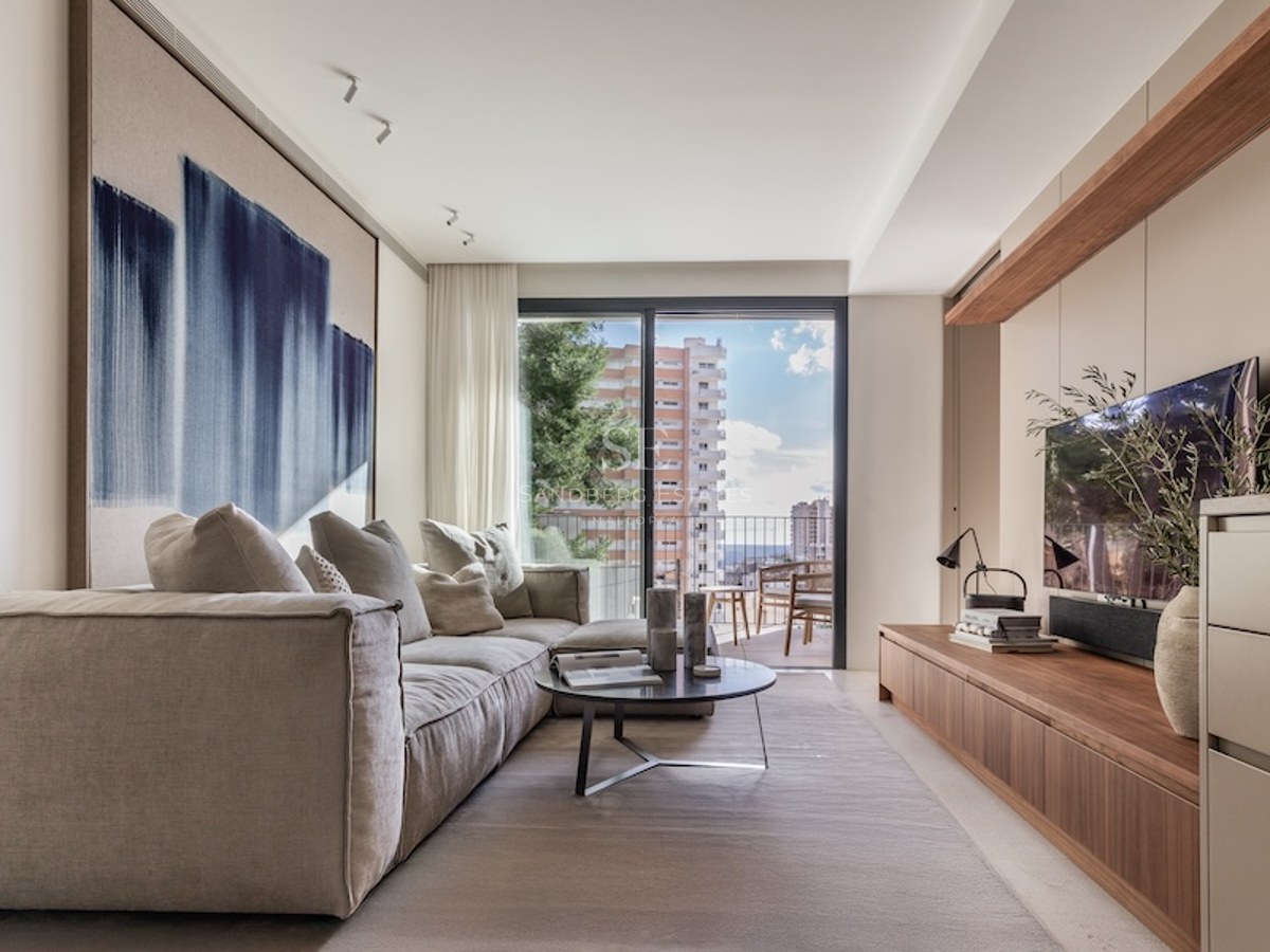 Bright modern living room featuring a plush beige sofa, abstract blue art, wooden TV console, and a balcony view.