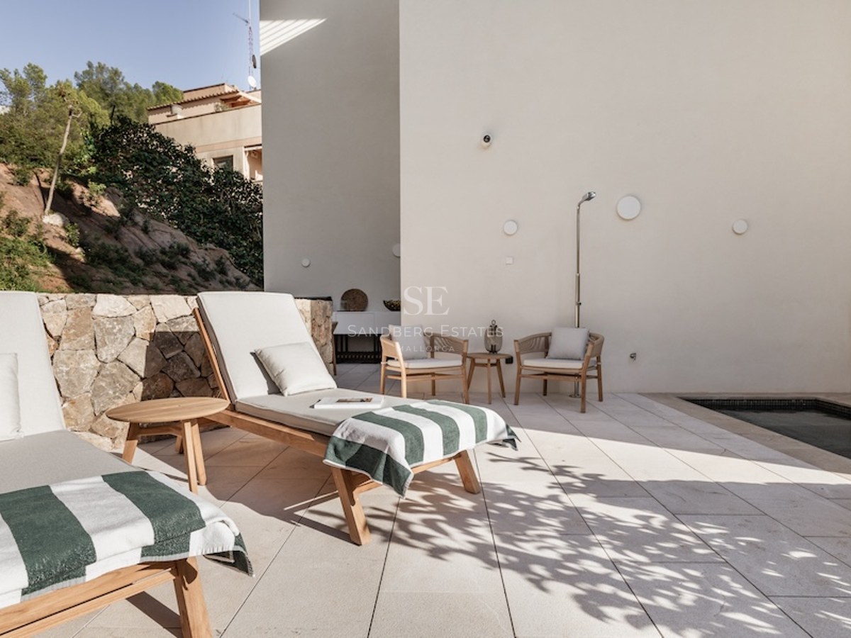 Modern outdoor terrace featuring wooden sunbeds, a small plunge pool, and a natural stone wall in bright sunlight.