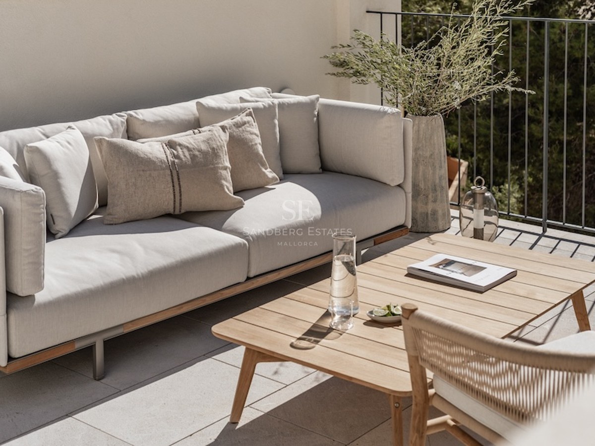 Moderne Terrasse mit einem grauen Sofa, Holztisch und dekorativen Pflanzen in mediterranem Ambiente.