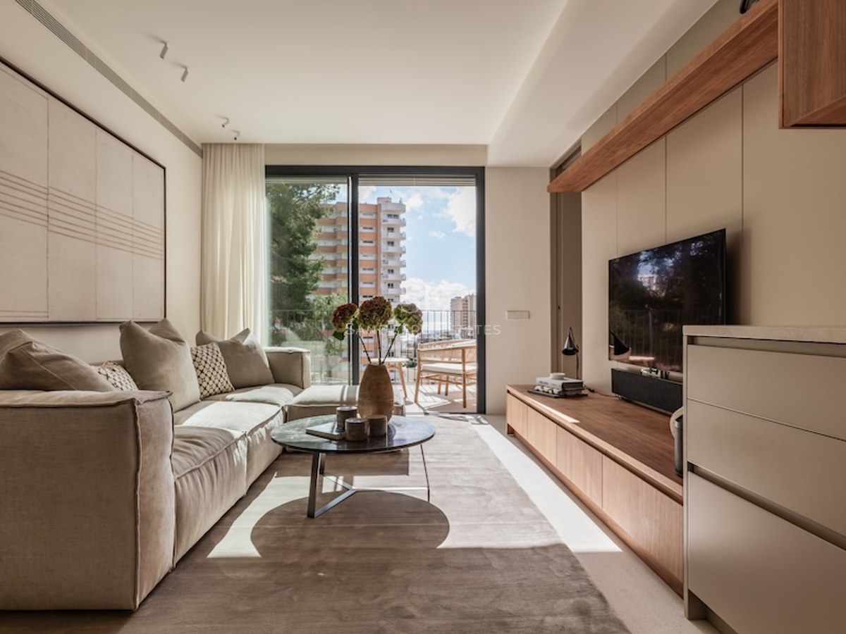 Helles Wohnzimmer mit großem beigem Sofa, Marmor-Couchtisch und Glasschiebetüren zum Balkon.