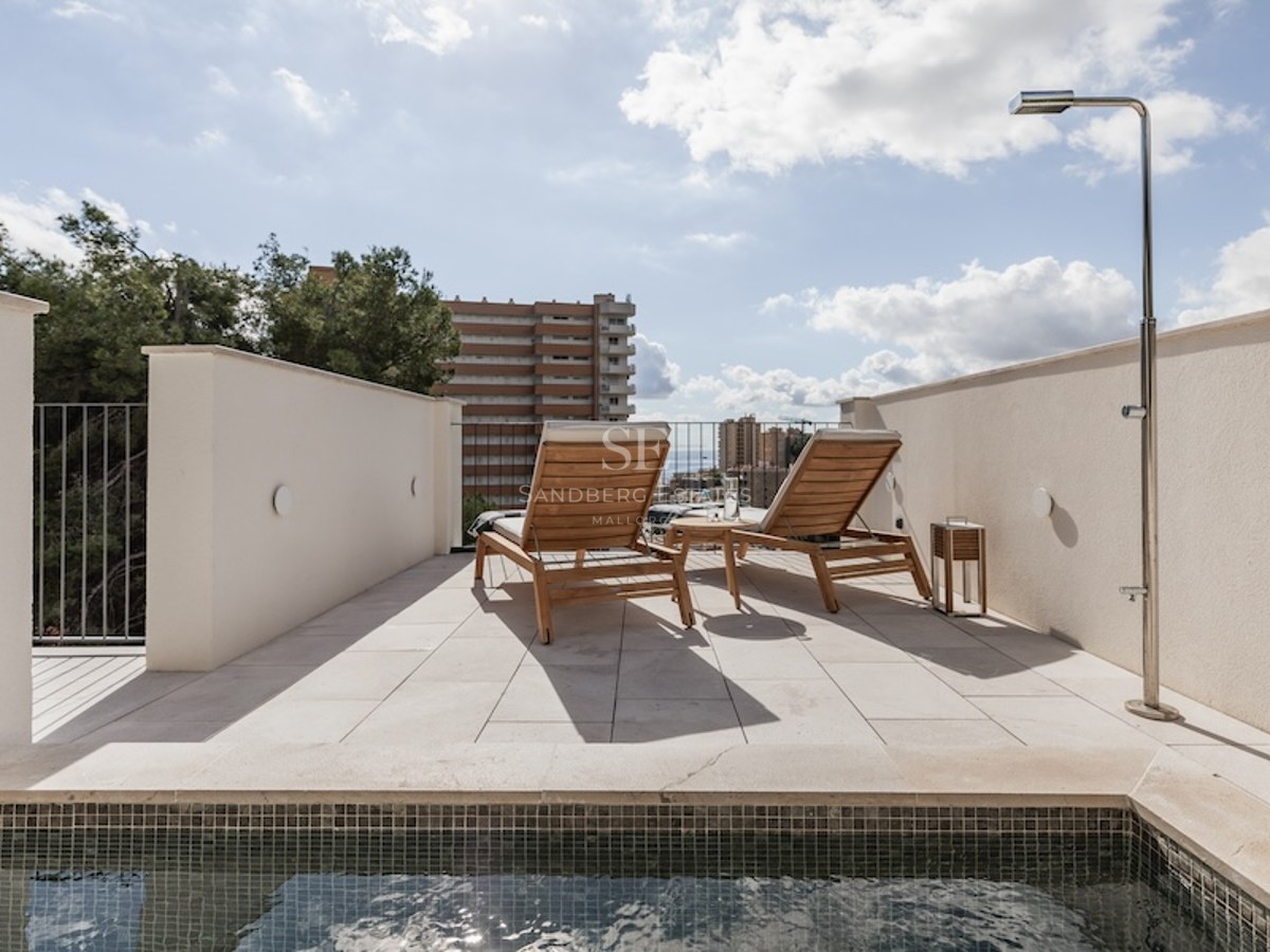 Sonnige Terrasse mit kleinem Pool, zwei Sonnenliegen aus Holz und Außendusche unter blauem Himmel.