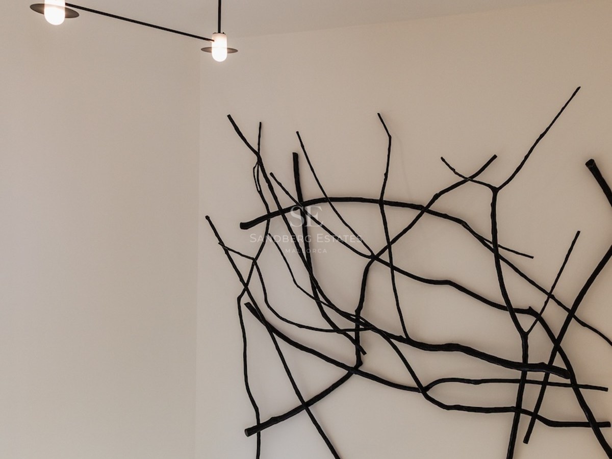 Schwarze, astähnliche Wandskulptur neben einem modernen Kronleuchter in einem weißen minimalistischen Raum mit Treppe.