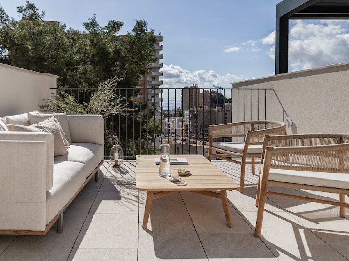 Luxuriöse Dachterrasse mit cremefarbenem Sofa, Holzsitzbänken und Blick auf die Stadt und das Meer unter blauem Himmel.