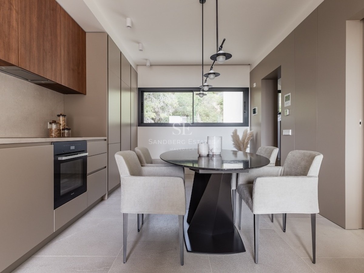 Modernes Esszimmer mit ovalem schwarzem Tisch, grauen Sesseln und taupefarbenen Schränken unter Designerleuchten.