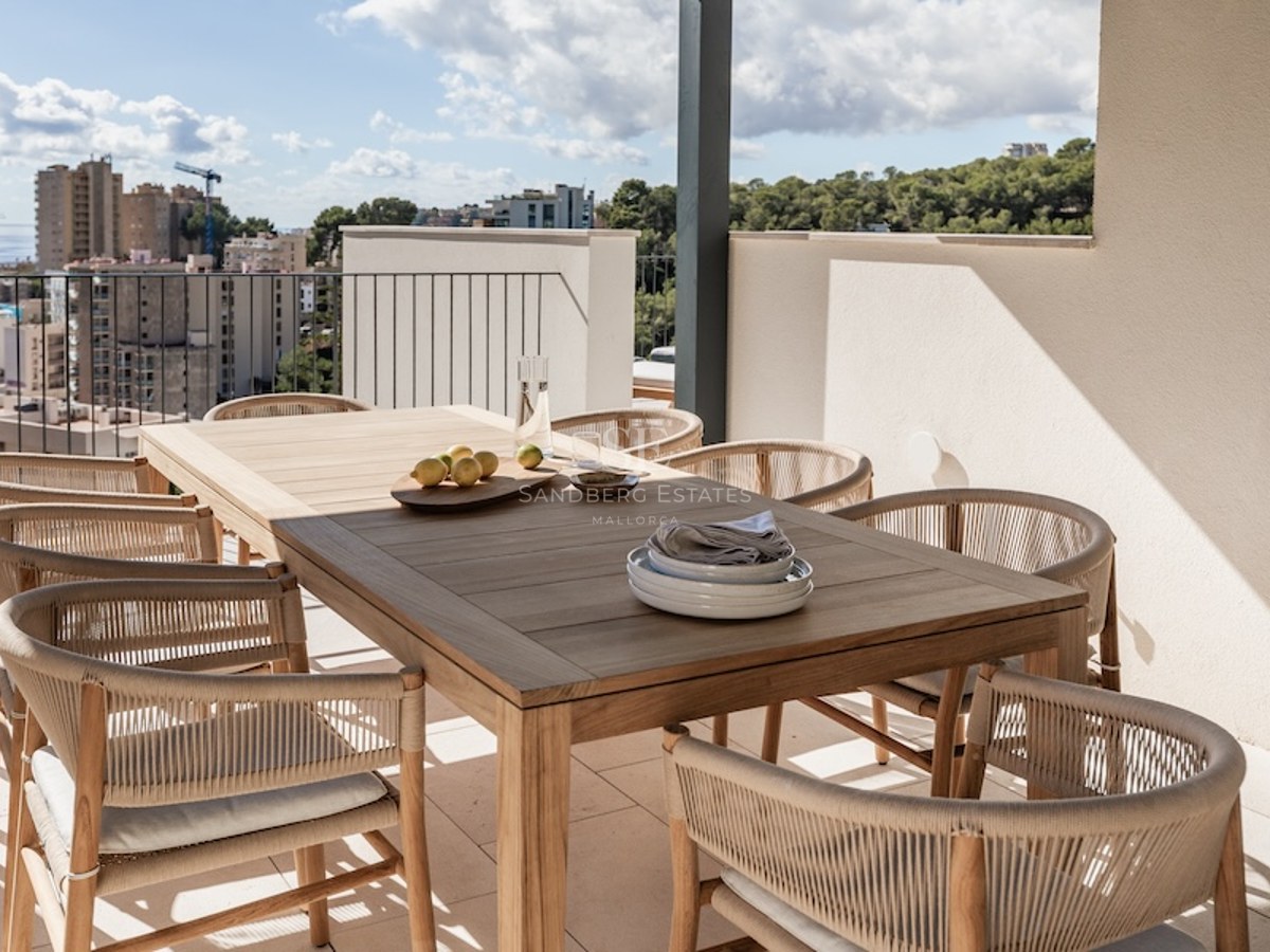 Moderne Terrasse mit Holztisch, geflochtenen Stühlen und Panoramablick auf Meer und Stadt.