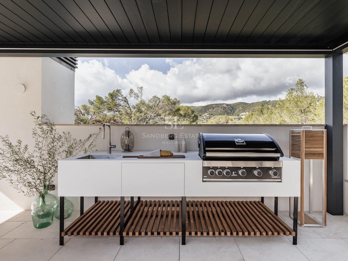 Moderne Außenküche mit Profi-Grill, Spüle und weißen Schränken auf einer Terrasse mit Blick auf die Berglandschaft.