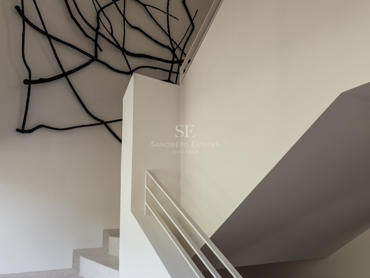 Weiße minimalistische Treppe mit einer schwarzen Ast-Skulptur an der Decke und den Wänden in einem hellen Raum.
