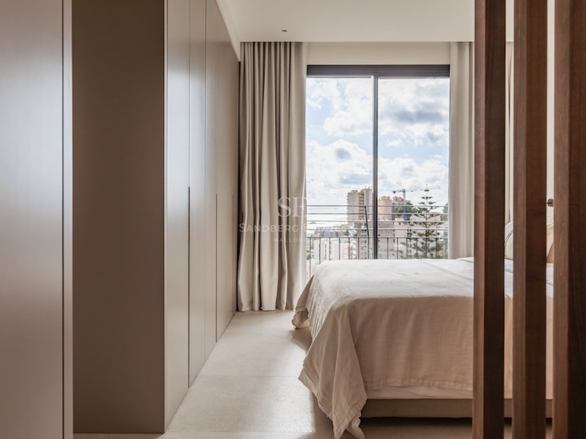 Helles Schlafzimmer in neutralen Tönen mit großem Einbauschrank und bodentiefem Fenster mit Blick auf die Stadt.