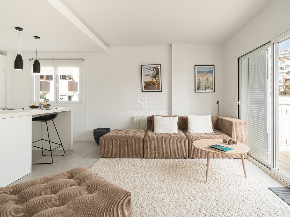Bright living room with brown corduroy modular sofa, white textured rug, kitchen island, and large glass doors to a balcony.