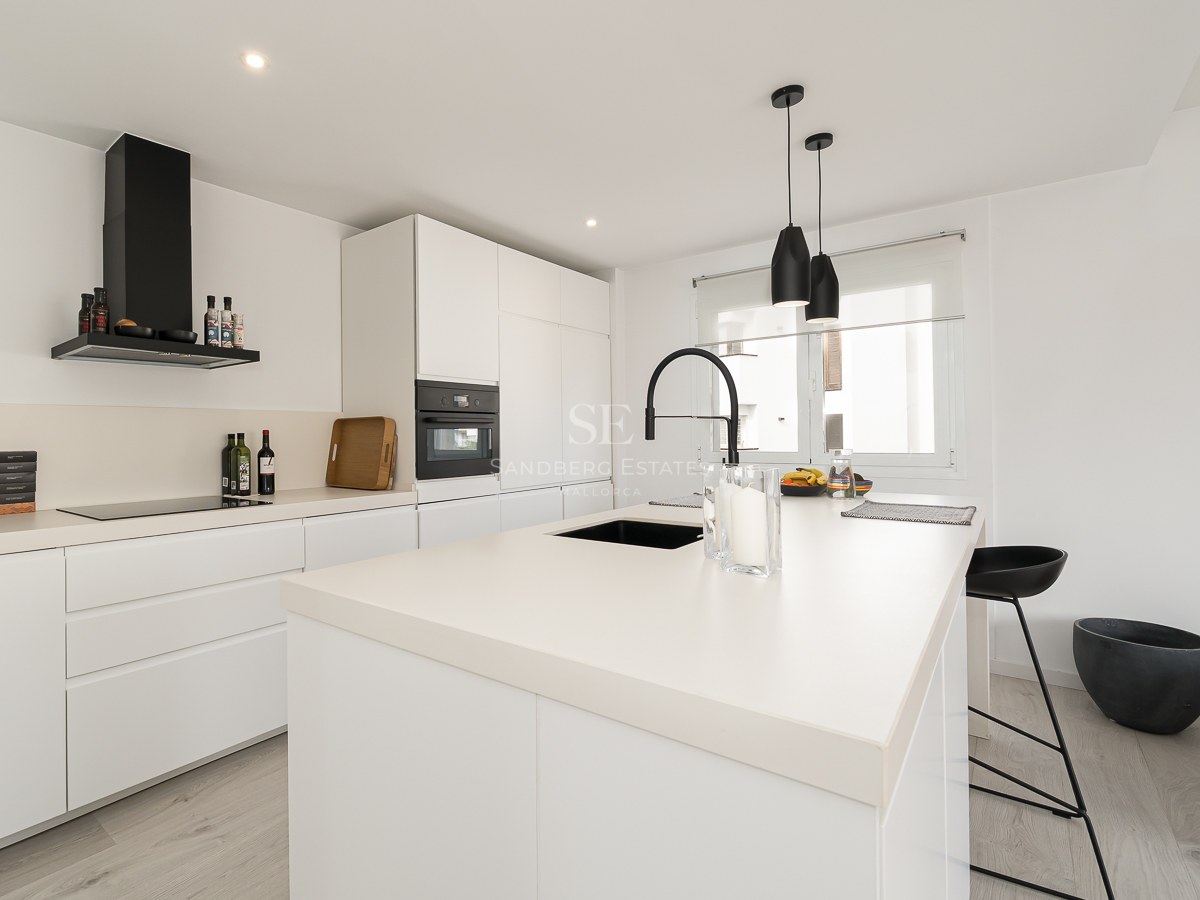 Modern white kitchen with a large island, black faucet, and sleek integrated appliances.
