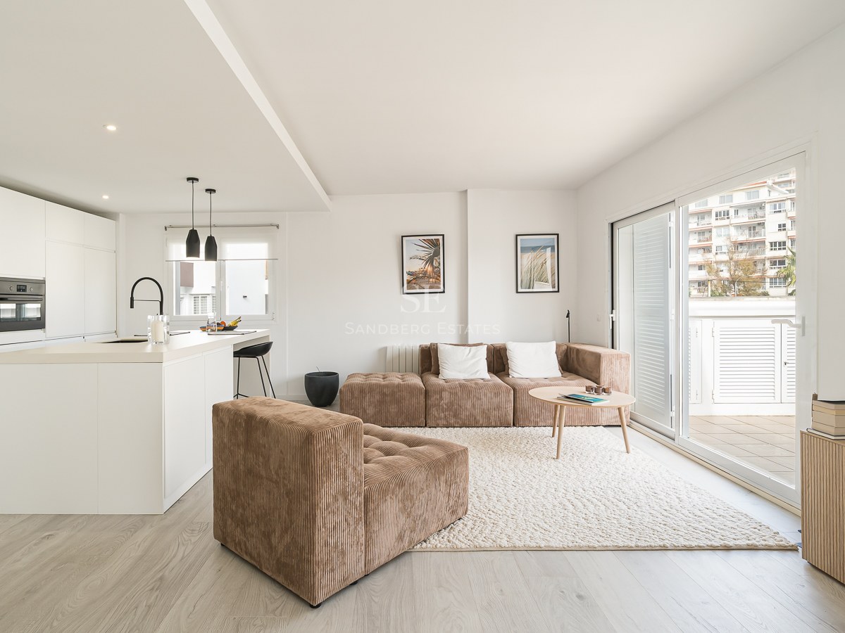 Bright modern living room with a brown corduroy modular sofa, textured rug, and a minimalist white kitchen.