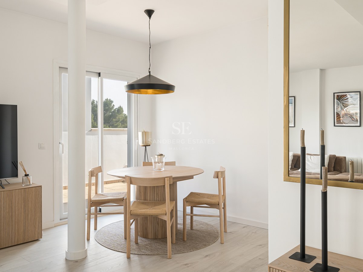 Bright dining area featuring a round wooden table, wicker chairs, black pendant lamp, and terrace access.