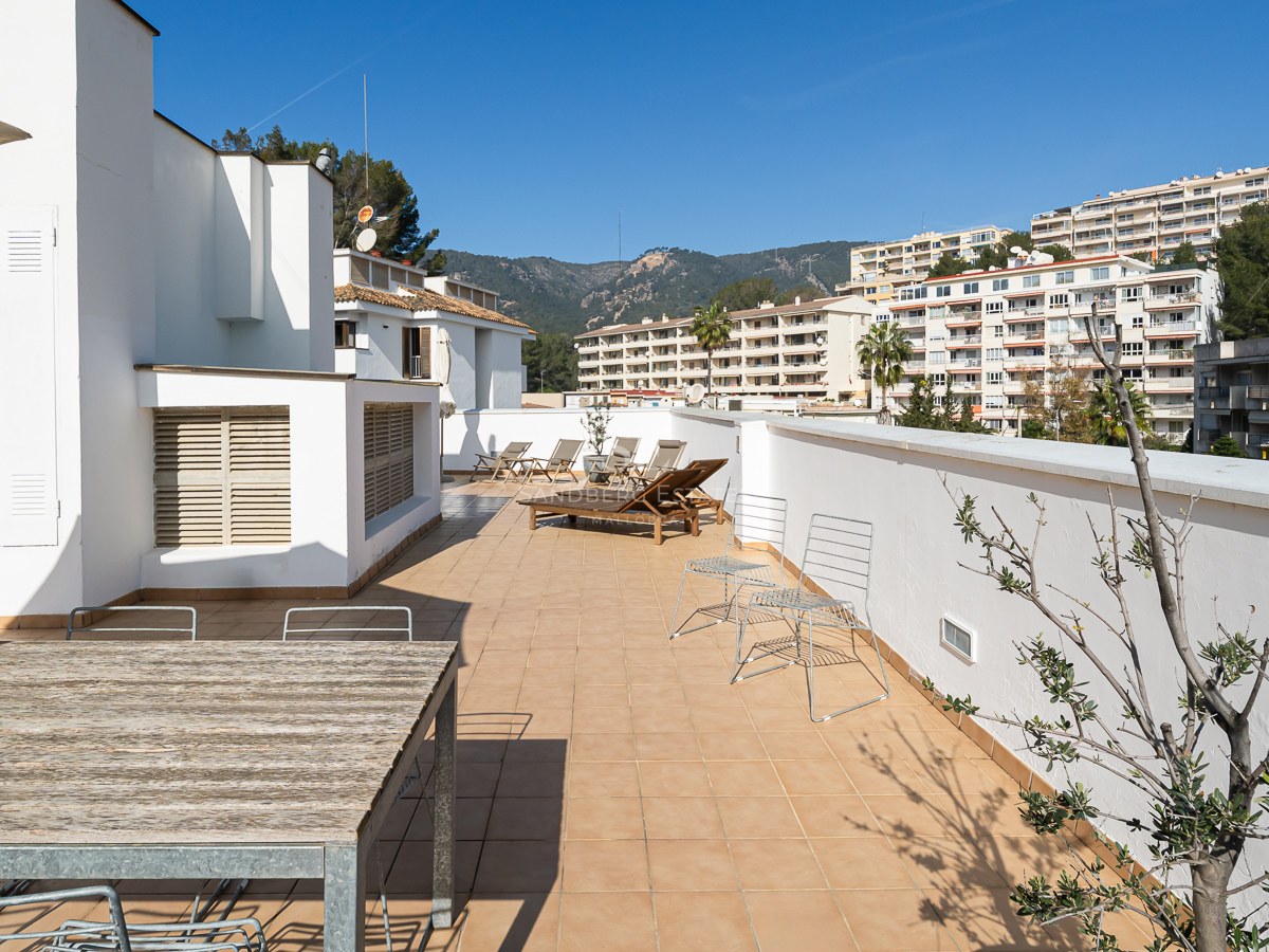 Large terrace with terracotta tiles, wooden sun loungers, and dining table under a clear blue sky.