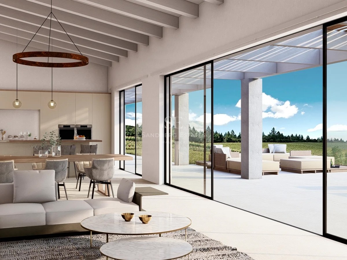 Bright living room with wooden beams, modern sofas, and large glass sliding doors opening to a sunny terrace.