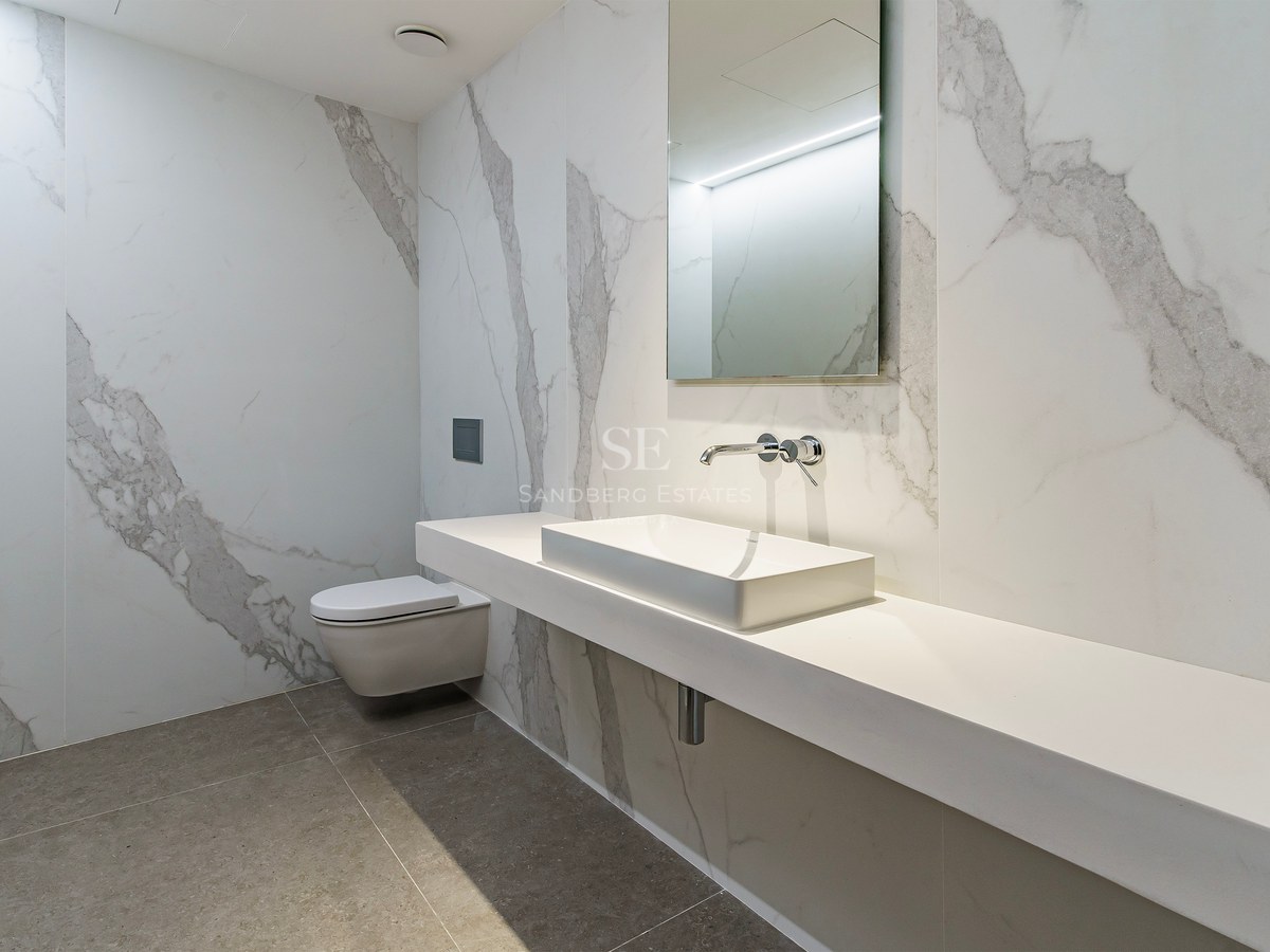 Baño moderno con revestimiento de mármol blanco, lavabo rectangular suspendido y grifería cromada empotrada.