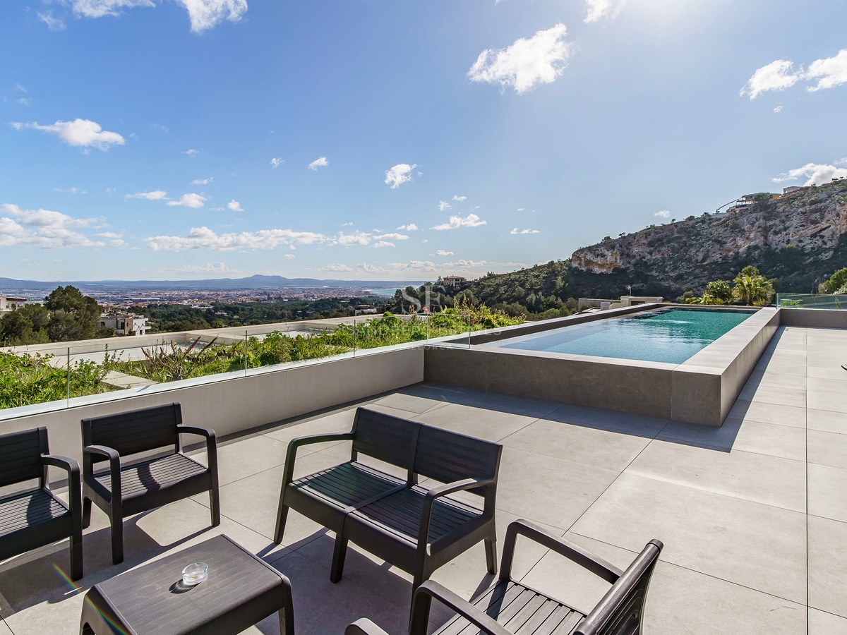 Terraza de lujo con piscina infinita, barandillas de cristal, muebles negros y vistas panorámicas al mar.