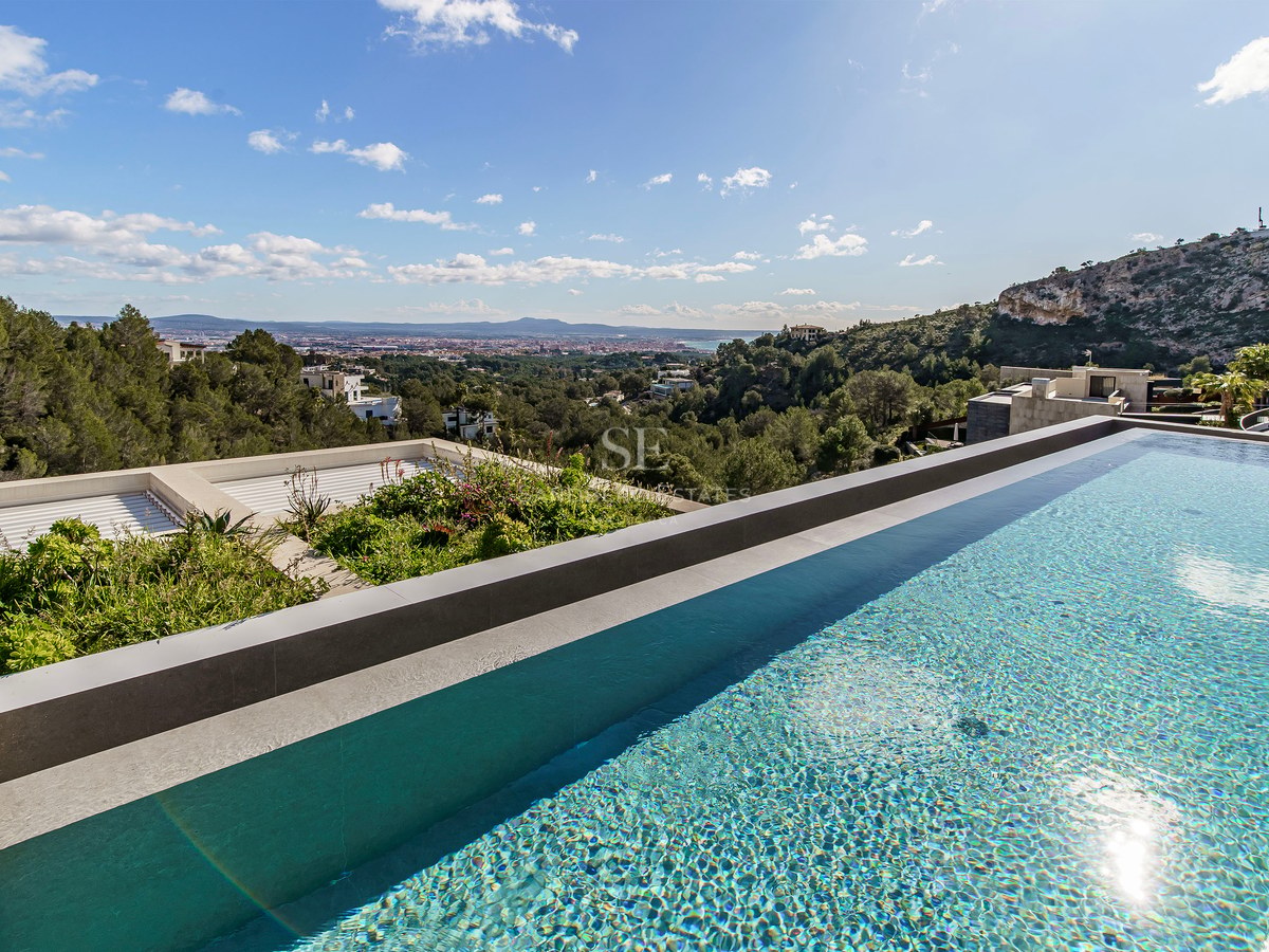 Piscina infinita con agua cristalina con vistas a un valle verde y una ciudad lejana bajo un cielo despejado.
