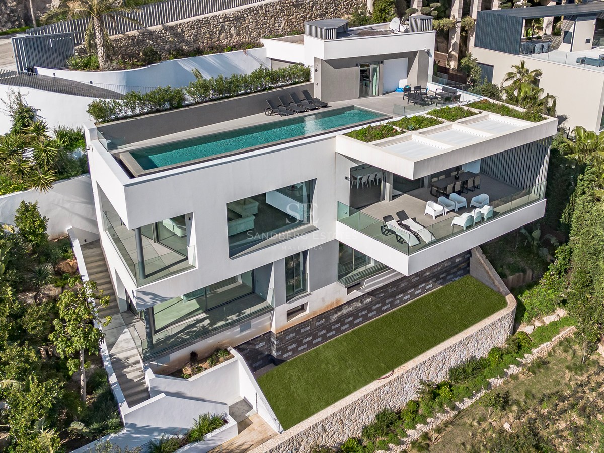 Vista aérea de una villa blanca de tres niveles con piscina infinita en la azotea y terrazas de cristal.