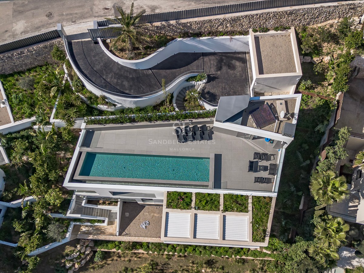 Vista aérea de una villa blanca moderna con piscina rectangular, tumbonas y una rampa de entrada curva.