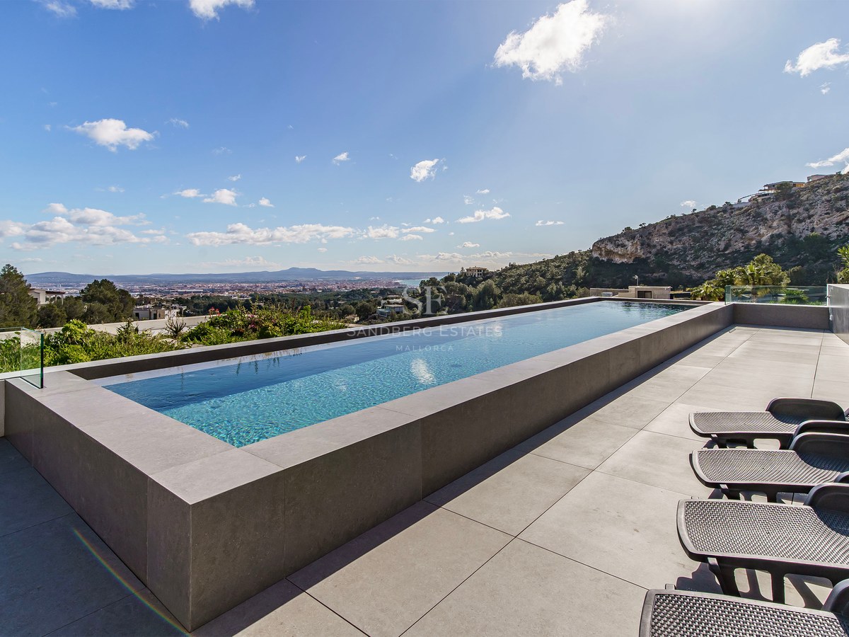 Piscina infinita en una terraza de piedra con tumbonas y vistas despejadas a la ciudad y la montaña.