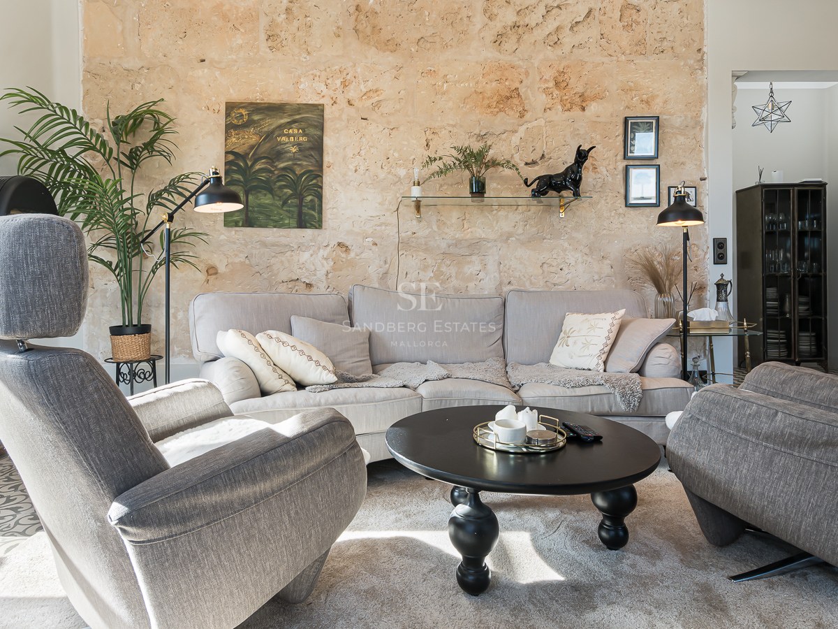 Modernt vardagsrum med grå fåtöljer, beige soffa, svart soffbord och en stor rustik stenvägg.