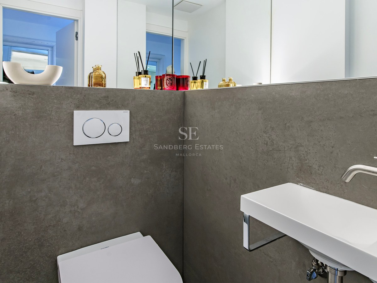 A minimalist bathroom featuring grey stone-effect walls, a slim white wall-mounted sink, and a large mirror.