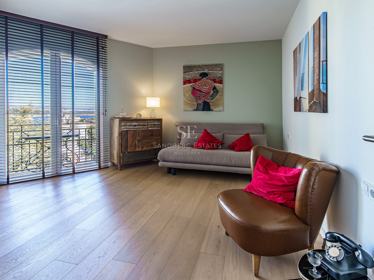 Contemporary bedroom with oak floors, a brown leather chair, sofa bed, and glass doors opening to a balcony.
