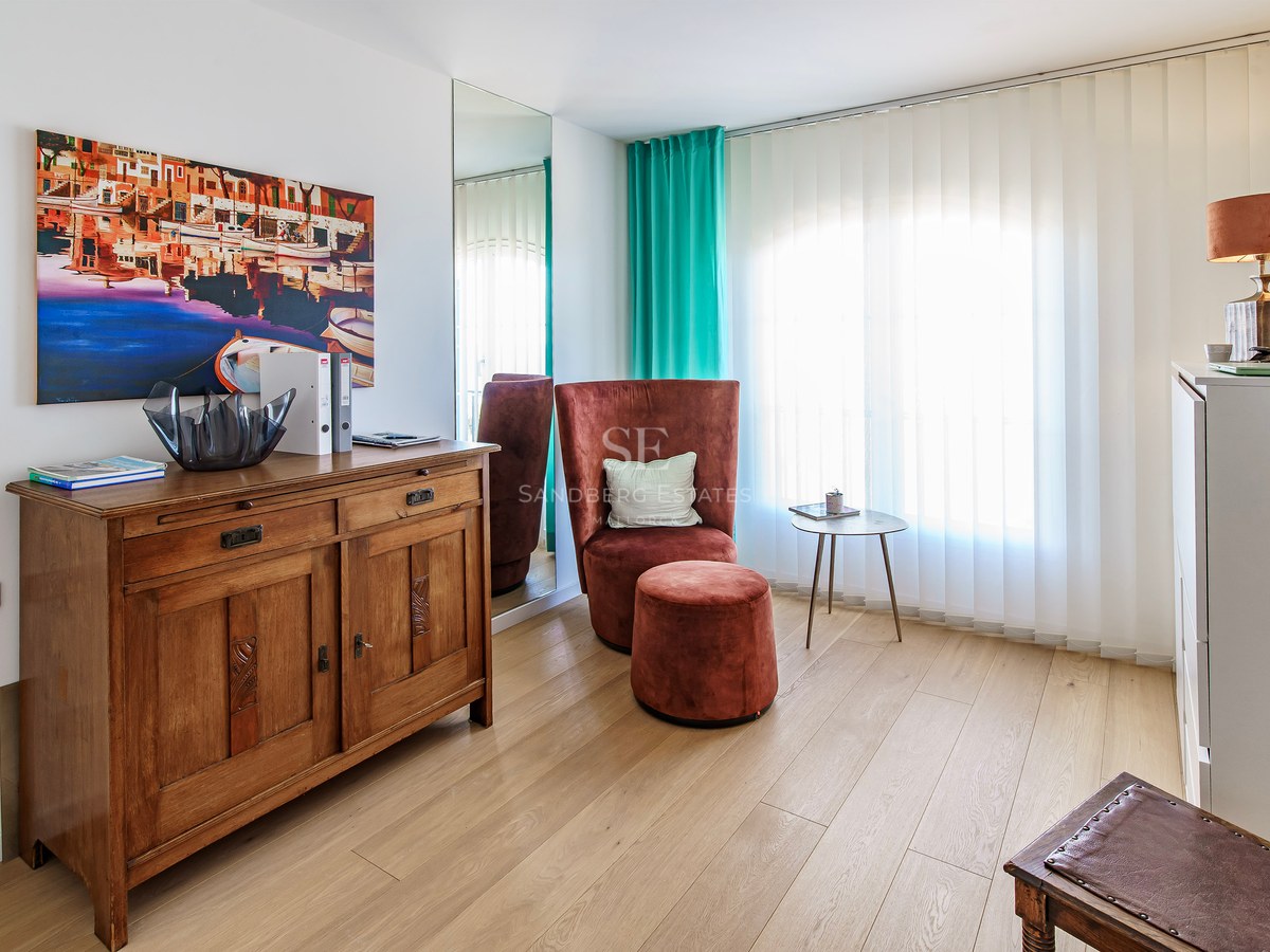 Cozy seating area with a terracotta velvet chair, wooden sideboard, and coastal artwork on light wood flooring.