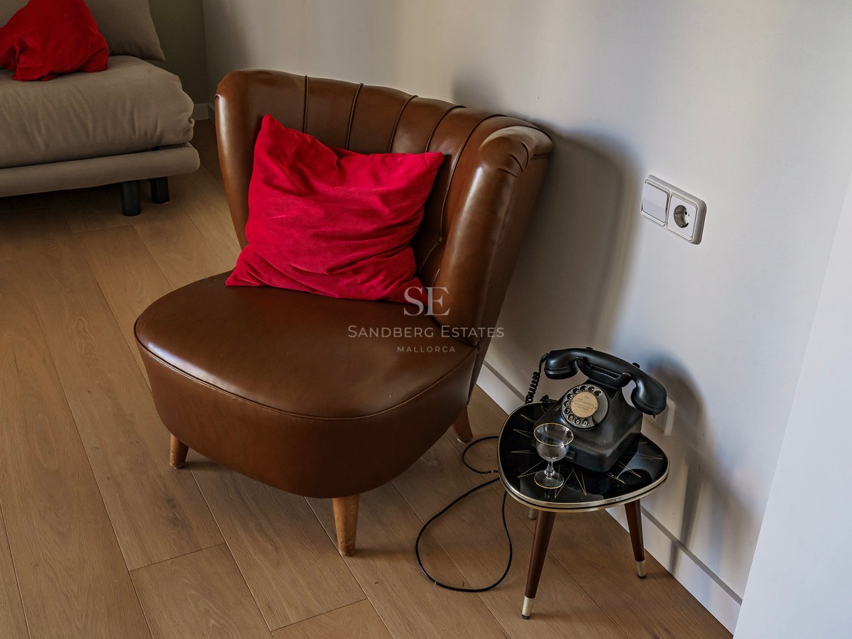 Fauteuil en cuir marron avec coussin rouge à côté d'un téléphone à cadran vintage sur une table basse.