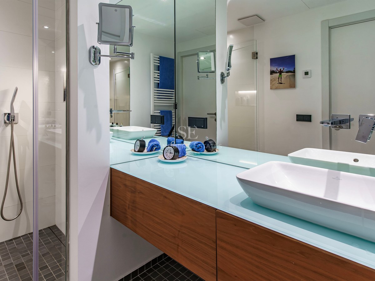 Modern bathroom featuring a white vessel sink on a floating wood vanity next to a walk-in shower with mosaic floor.