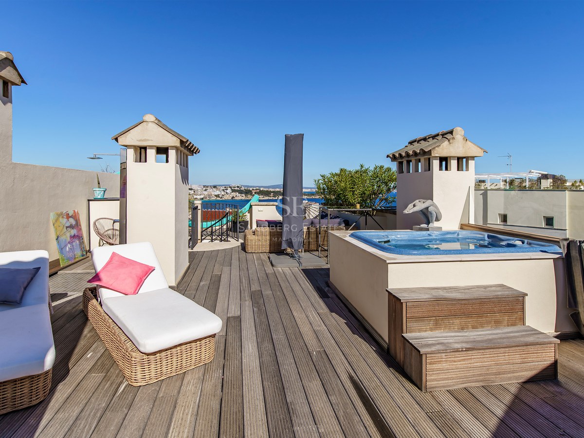 Rooftop wooden deck featuring a built-in hot tub, wicker sun loungers, and panoramic views of the Mediterranean coastline.