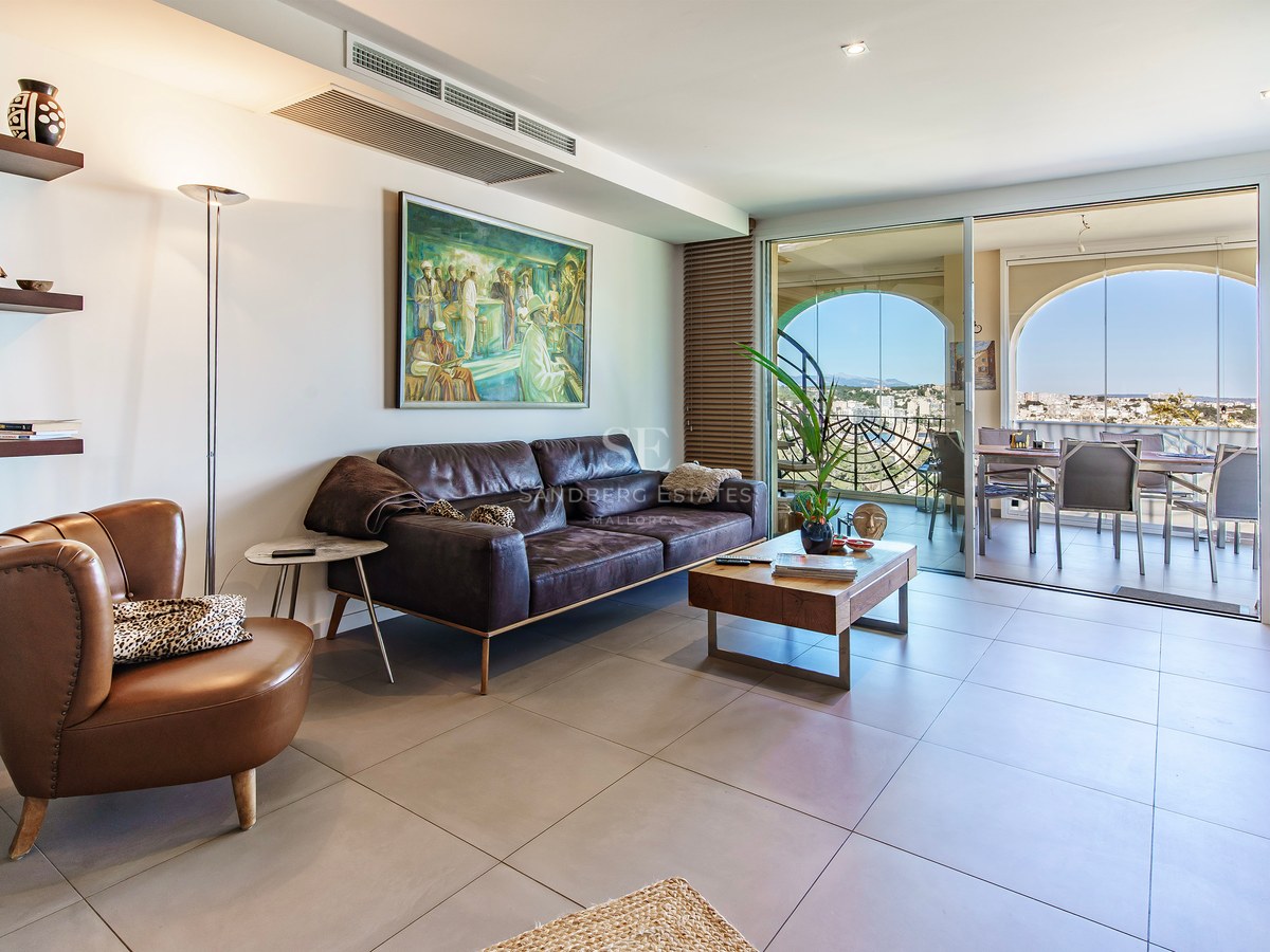 Modern living room with leather sofa and large glass doors opening to a terrace with panoramic coastal views.