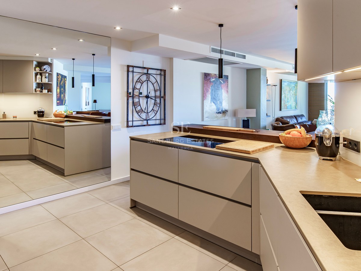 Contemporary open-plan kitchen with taupe cabinets, stone countertops, and a full-height wall mirror reflecting the room.