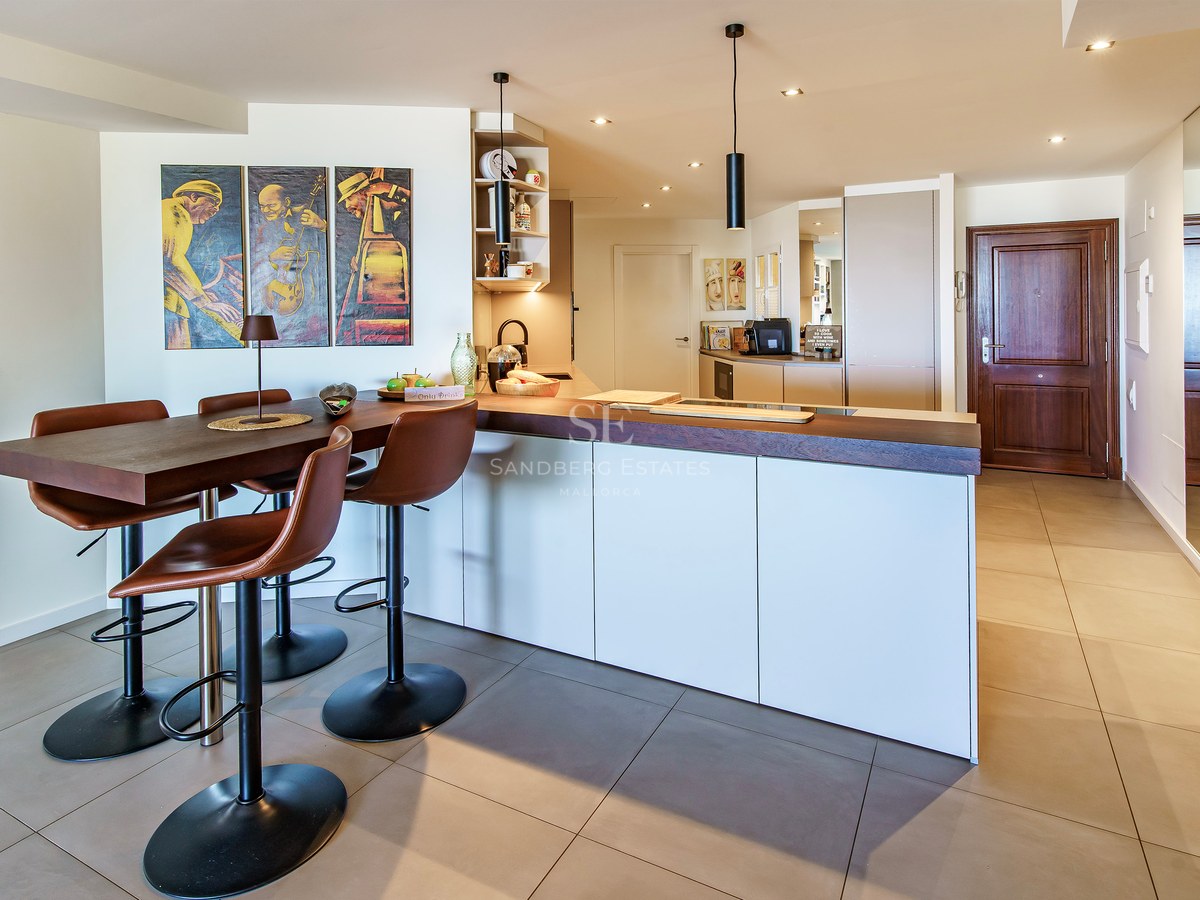 Modern white kitchen island featuring a dark wood breakfast bar and leather stools against a minimalist backdrop.