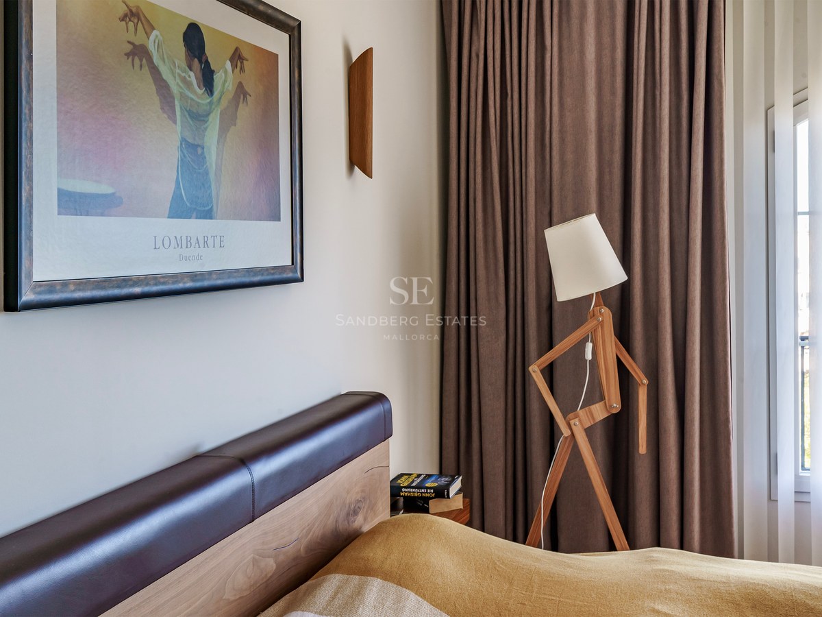 Gros plan d'une chambre avec une tête de lit en bois, un lampadaire design articulé et des rideaux taupe.